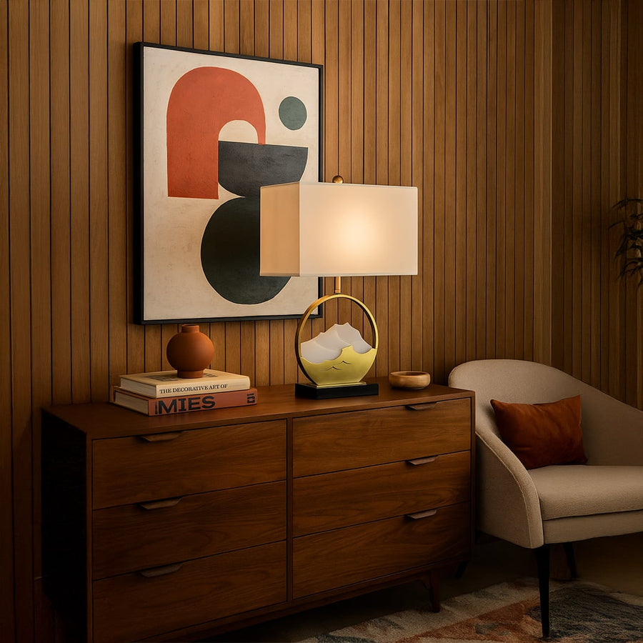 Table lamp with gold metal frame black base and rectangular fabric shade styled on a wooden dresser creating warm ambient lighting in a modern living space.