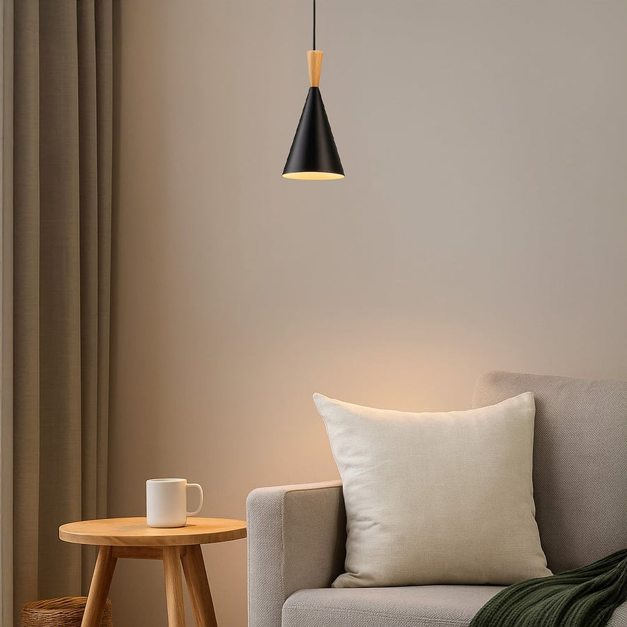 Modern black metal and light wood pendant light fixture hanging over a grey sofa and wood side table in a cozy living room setting.