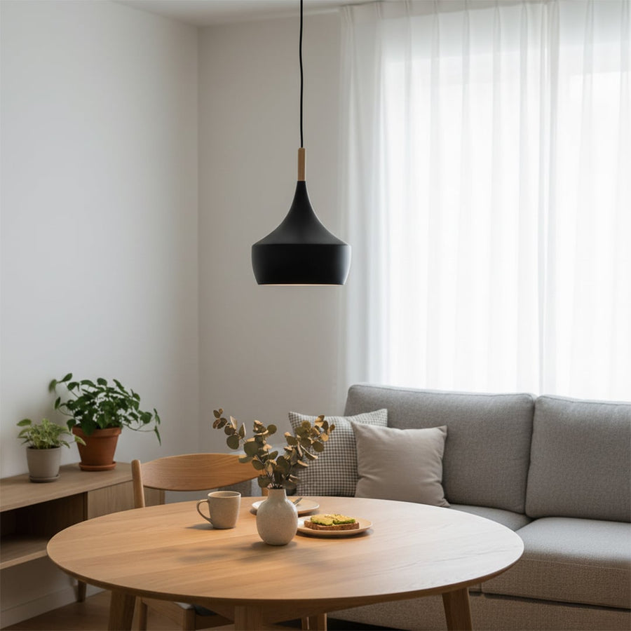 Modern black metal cone pendant light with wood top hanging over a small wood side table in a warm cozy living room corner for home decor.