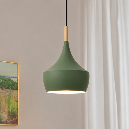 A modern pendant light with a matte sage green shade, a light natural wood neck, and a black cord, shown hanging in a room with white curtains and a framed landscape painting on the wall.