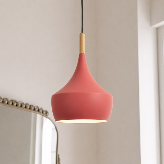 A modern teardrop-shaped pendant light with a matte coral pink shade, a light natural wood neck, and a black hanging cord, shown in a softly lit interior setting.