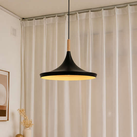 A modern black pendant light with a warm yellow glow, featuring a light wood accent near the top, hanging in front of sheer white curtains.