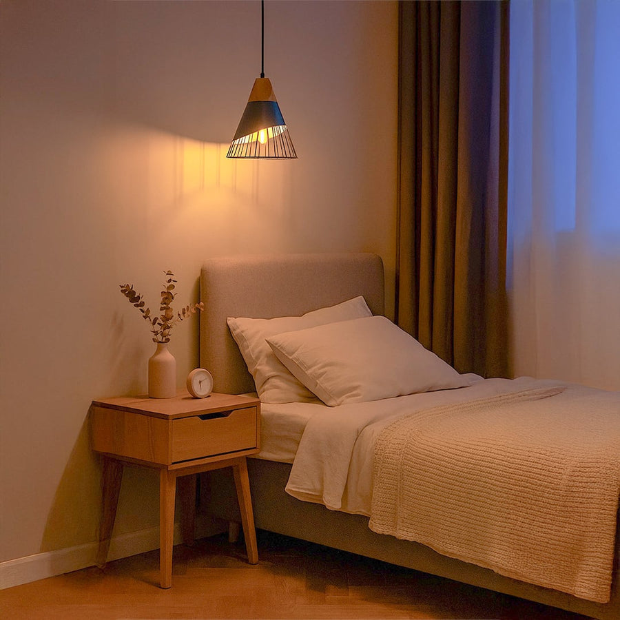Black metal cage pendant light with wood accent illuminating cozy bedroom with warm ambiance.