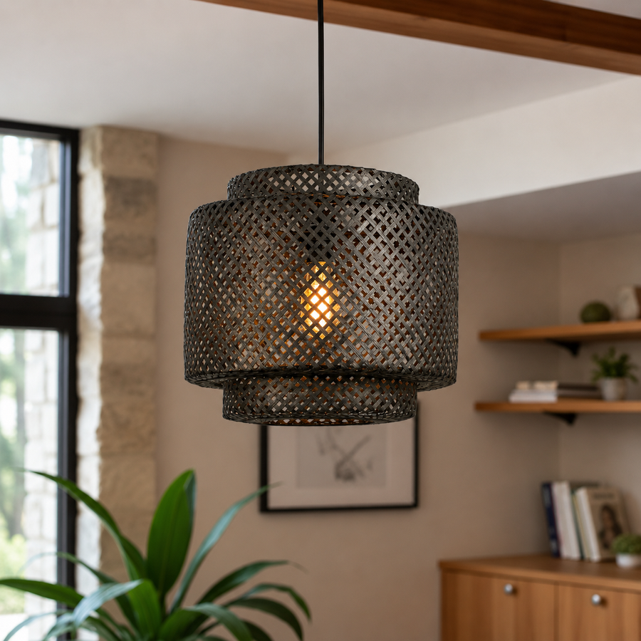 A dark metal pendant light with a cylindrical, open-lattice shade hangs in a warm, modern room setting with a wooden ceiling beam, shelves, and a plant in the background.