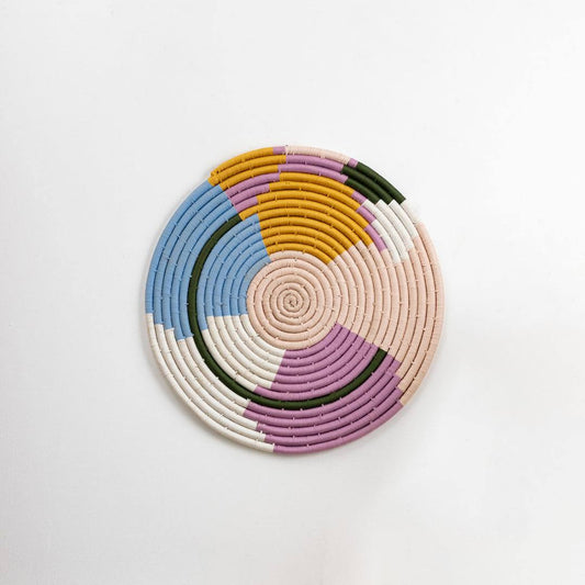 Round handcrafted pastel seagrass wall basket with purple blue cream and mustard pattern on white background image.