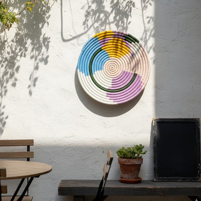Handmade round wall decor with multicolor pattern mounted on outdoor wall adding playful artistic touch to patio seating area.
