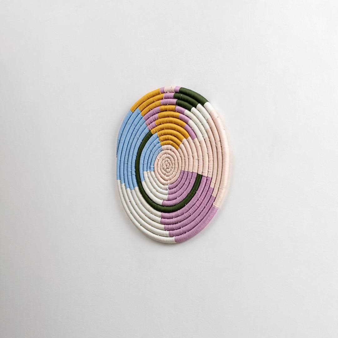 Round handcrafted pastel seagrass wall basket with colorful woven pattern on white background image.