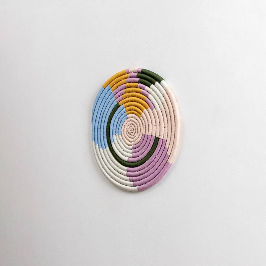 Round handcrafted pastel seagrass wall basket with colorful woven pattern on white background image.