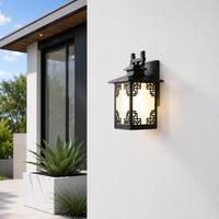 Ornate black metal outdoor wall lantern with patterned glass on white stucco facade for elegant porch entryway lighting.
