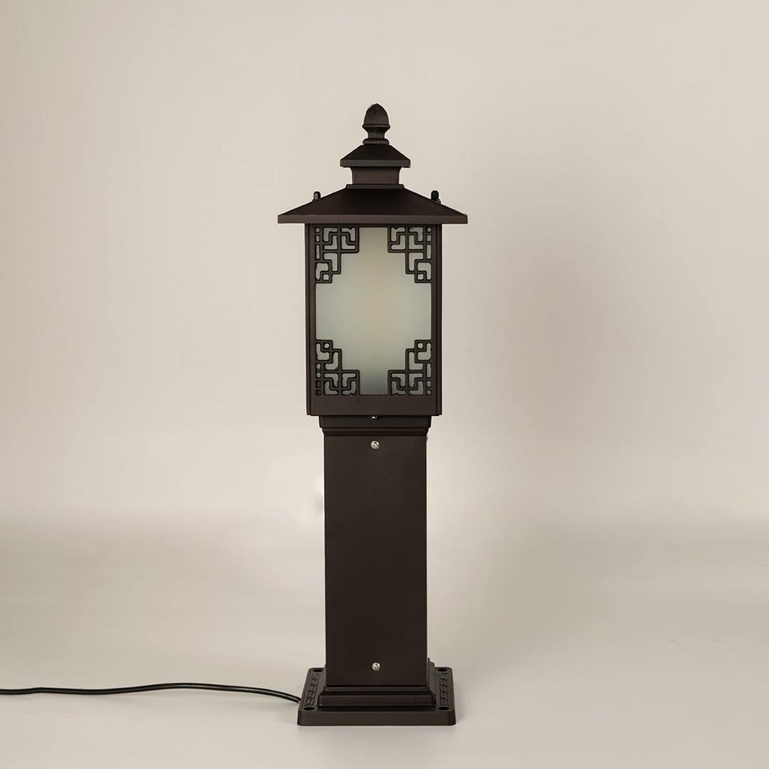 A decorative outdoor bollard light photographed on a white background with the light off highlighting the detailed metal design and frosted glass panels in a clear studio view.