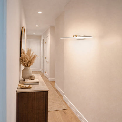 Gold metal picture light enhancing hallway artwork with warm illumination creating sophisticated interior ambiance.