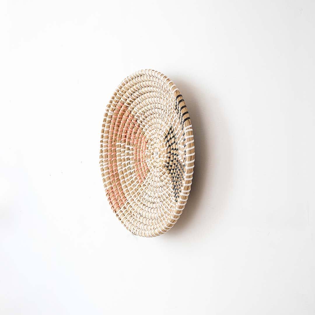 Side angle view of a geometric woven seagrass wall hanging basket plate showing the texture depth on a white wall.