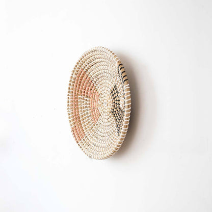 Side angle view of a geometric woven seagrass wall hanging basket plate showing the texture depth on a white wall.