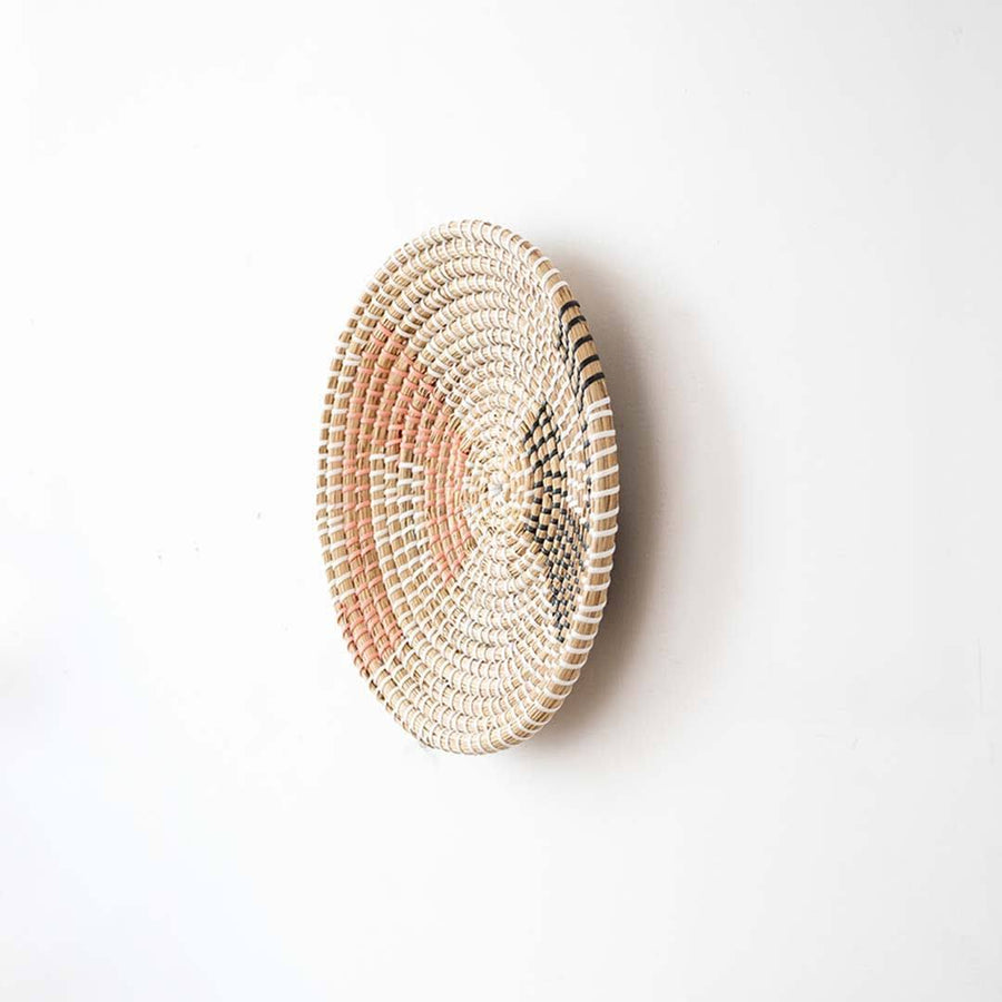 Side angle view of a geometric woven seagrass wall hanging basket plate showing the texture depth on a white wall.