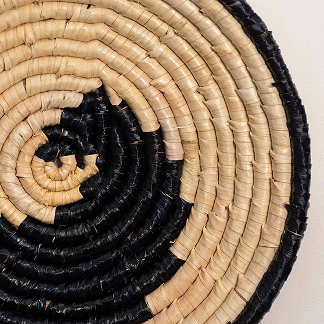 Detailed closeup of handcrafted black cream seagrass wall basket with woven yin yang spiral pattern for artisan home decor.