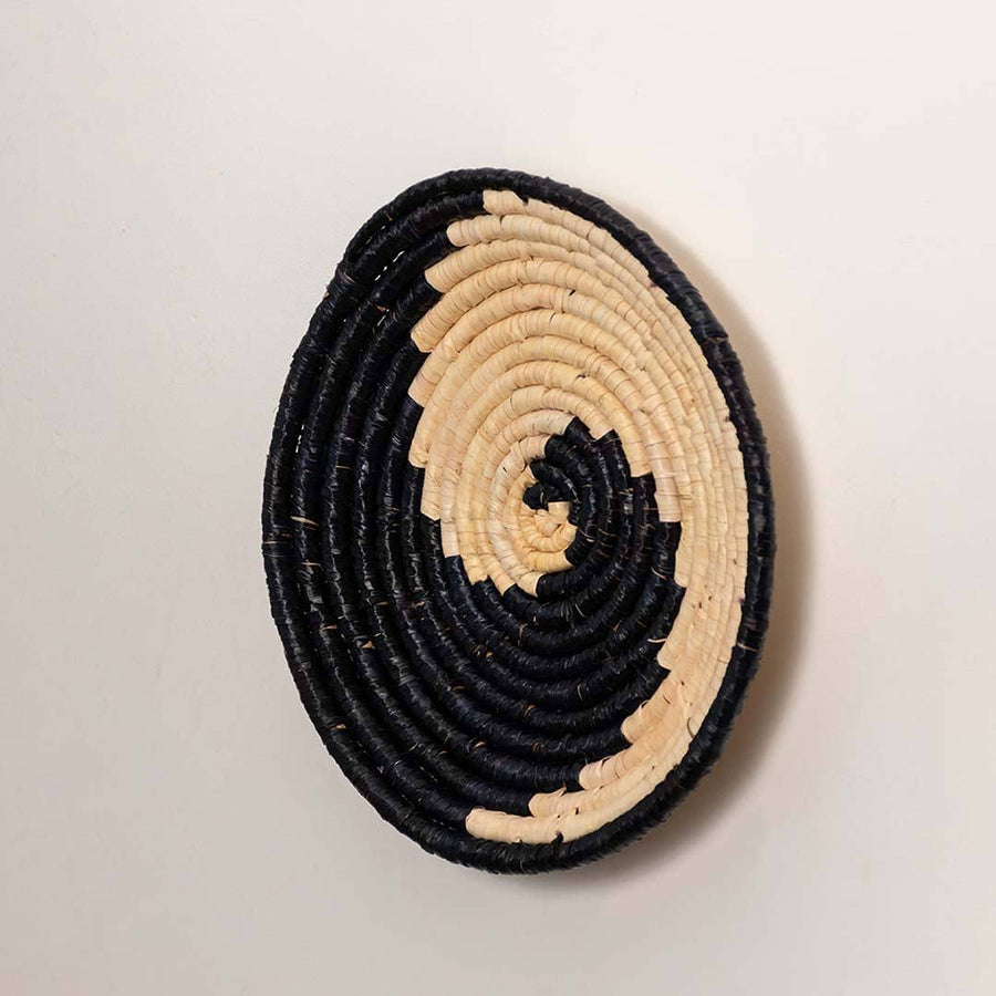 Side view of handcrafted black cream seagrass wall basket with yin yang spiral wave pattern for bohemian wall decor styling.