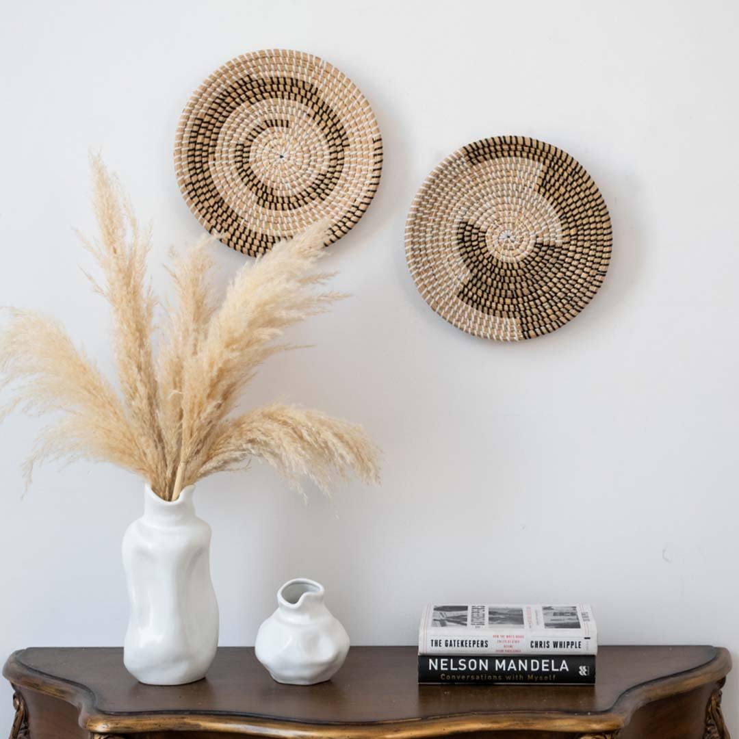Handwoven seagrass wall baskets styled above dark wood console table with pampas grass and ceramic vase for living room decor.