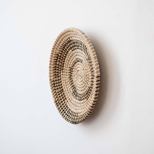 Side profile view of round handwoven natural fiber wall basket with black geometric woven accents for boho home wall decor.