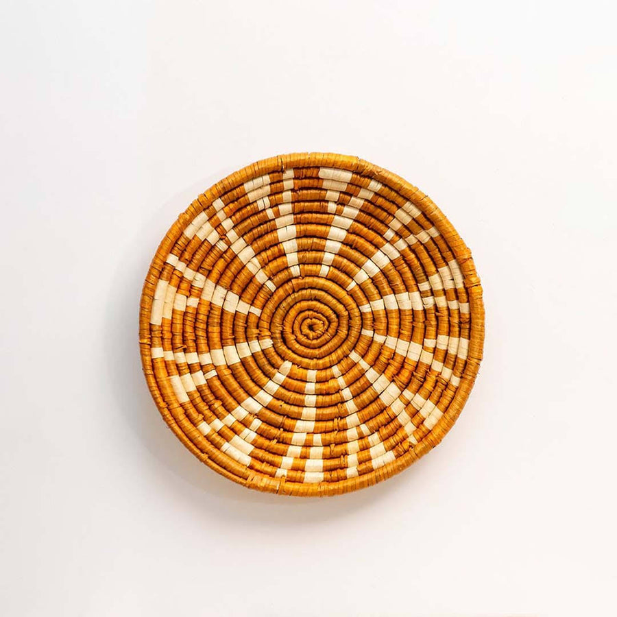 Handwoven seagrass round wall basket decor in natural beige and terracotta with sunburst woven pattern on white background.
