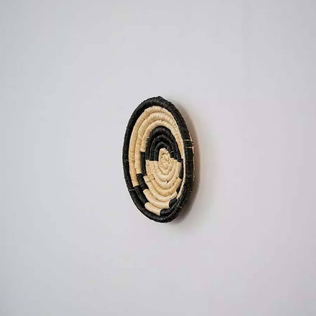 Handwoven seagrass round wall basket decor in natural beige and black with raised spiral woven profile on white.