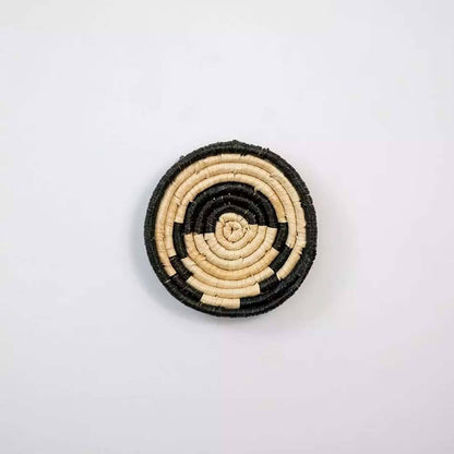 Handwoven seagrass round wall basket decor in natural beige and black with abstract spiral woven pattern on white background.