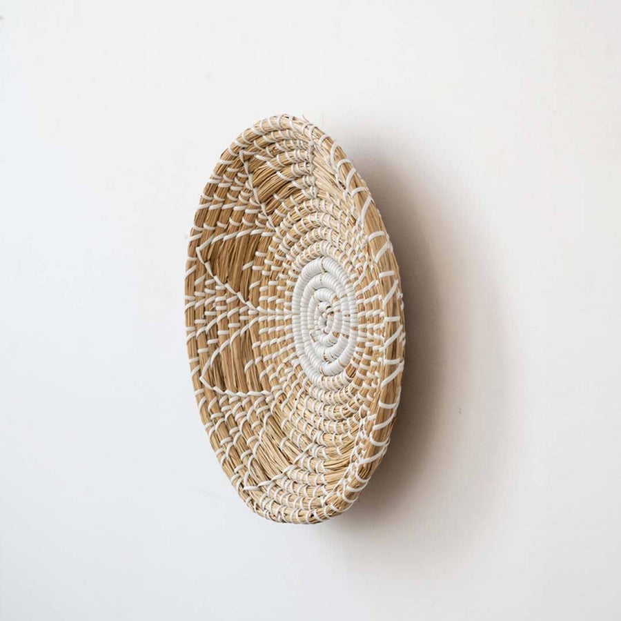 Handwoven seagrass round wall basket decor in natural beige with white spiral woven profile displayed from side on white.
