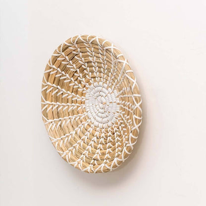 Handwoven seagrass round wall basket decor in natural beige with white spiral woven profile displayed on white background.