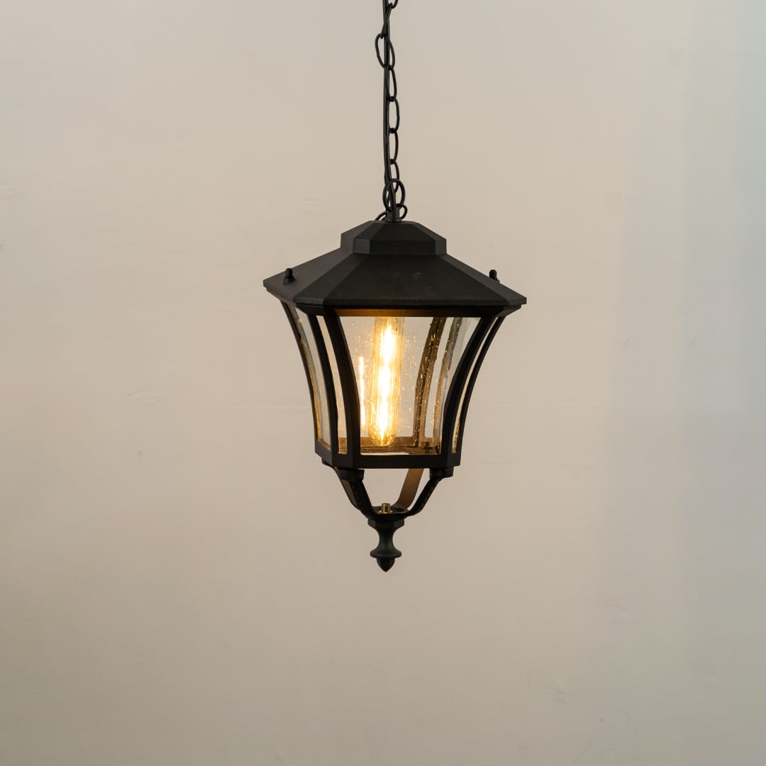 Black hanging outdoor lantern on white background with light on showing glowing textured glass panels and classic lantern top perfect for porch and entry lighting.
