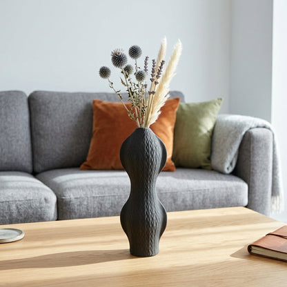 Black textured ceramic flower vase with dried blooms placed on table for modern home decor styling.