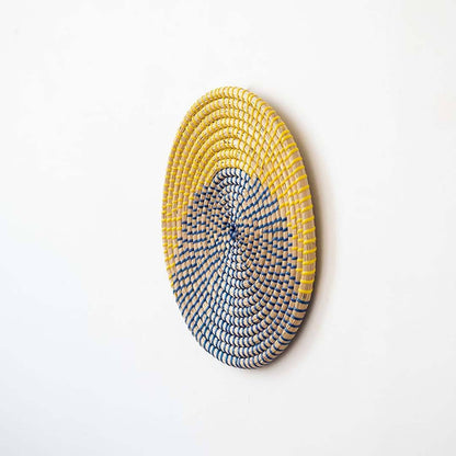 Handwoven seagrass round wall basket decor in yellow and charcoal with raised woven profile shown on white background.