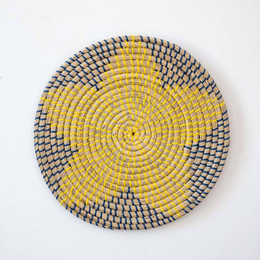 Handwoven seagrass round wall basket decor in yellow and charcoal with bold floral woven pattern on white background.