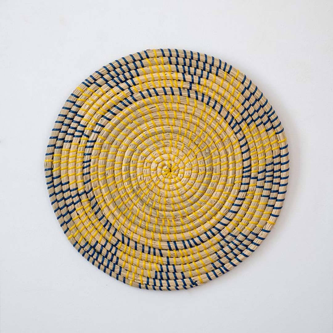 Handwoven seagrass round wall basket decor in yellow and charcoal with geometric woven pattern on white background.