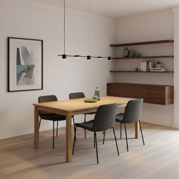 A modern dining room featuring a long black linear ceiling light hanging above a wooden table with four dark chairs in a warm minimalist interior.