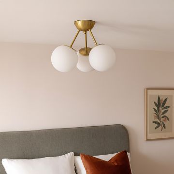 Modern gold ceiling light with three frosted glass globes glowing warmly above bed for elegant bedroom ceiling lighting.
