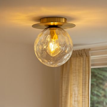 Modern gold ceiling light with clear textured glass globe glowing warmly in living room for stylish home ceiling lighting.