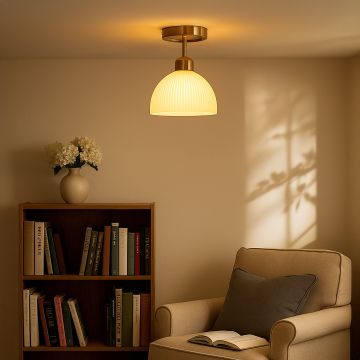 Modern ceiling light with brushed gold base and ribbed white glass shade styled in reading corner for warm home lighting.