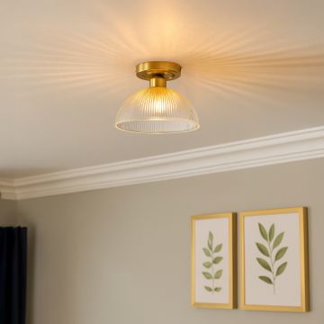 Modern ceiling light with brushed gold base and ribbed glass dome shade glowing warmly in living room interior decor.