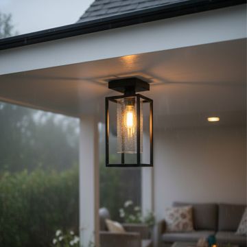 Black metal outdoor ceiling light with clear glass shade glowing warmly in a covered patio area creating a cozy inviting and weather safe ambience.