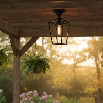 Black metal outdoor ceiling light with clear glass shade glowing warmly under a wooden pergola creating a cozy garden seating ambience at sunset.