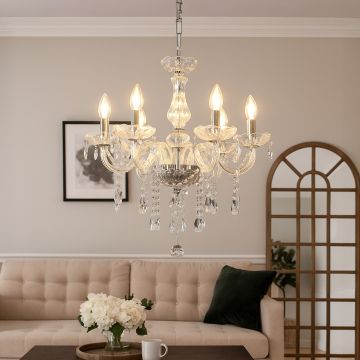 Crystal chandelier glowing warmly in a modern living room with beige sofa wall art mirror and floral table decor.