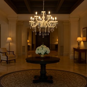 White chandelier with crystal detailing glowing in luxurious hotel lobby interior above round table with flowers.
