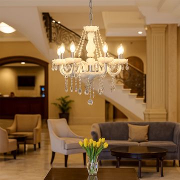 White chandelier with crystal droplets glowing in luxury lobby interior with seating and flowers for elegant decor.