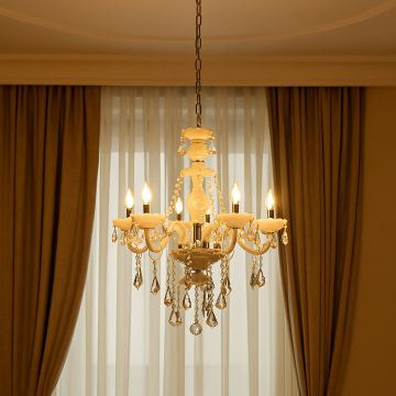 Elegant chandelier with crystal accents glowing warmly in living room with curtains and soft ambient lighting.