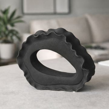 Dark grey ceramic abstract ring sculpture styled on console table for modern living room decor accent.