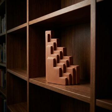 Orange ceramic stepped decorative sculpture displayed on wooden shelf creating warm and artistic interior decor accent.