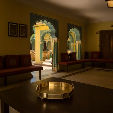 A decorative golden serving tray placed on a dark wooden table inside a traditional interior with carved arches and warm lighting creating an elegant cultural ambiance.