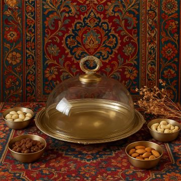 Elegant brass serving cloche displayed on a richly patterned backdrop with dry fruits arranged around it creating a warm festive lifestyle setting.