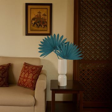 Teal dried palm leaf stems styled in a modern white vase on wooden side table in living room decor.