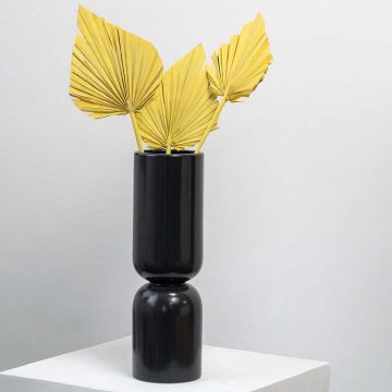 Yellow palm leaf decor in a black vase placed on a modern white pedestal perfect for living room or office decoration.