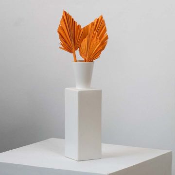 Orange dried palm leaves in white vase styled on modern table for boho home decor accent.